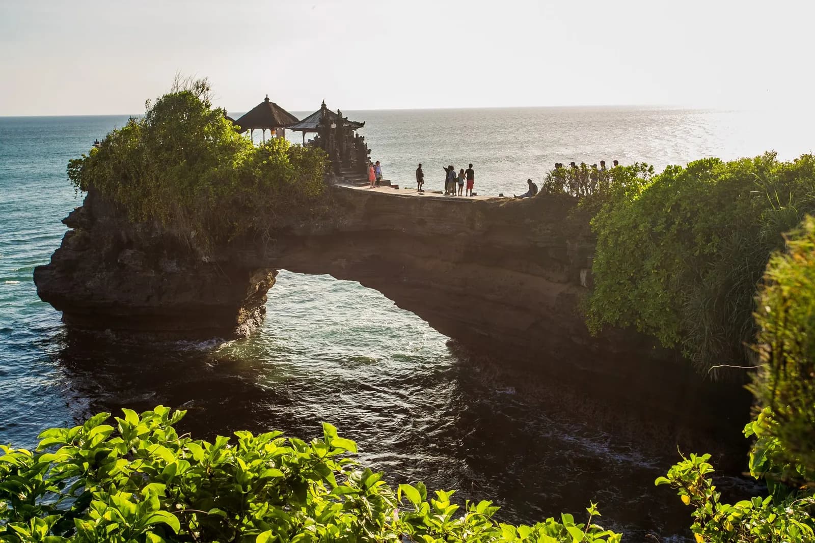 Batu Bolong temple standing on a rock arch with the sea running through the hole underneath it, Tanah Lot, Bali