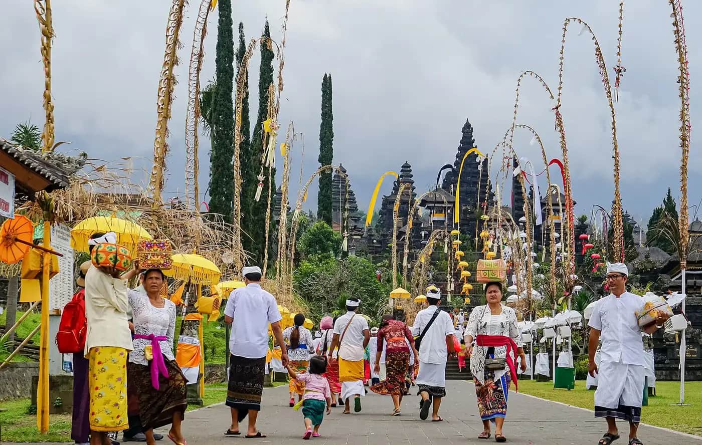 Balinese worshippers in ceremonial dress carrying offerings along the penjor-lined approach to Besakih on a festival day