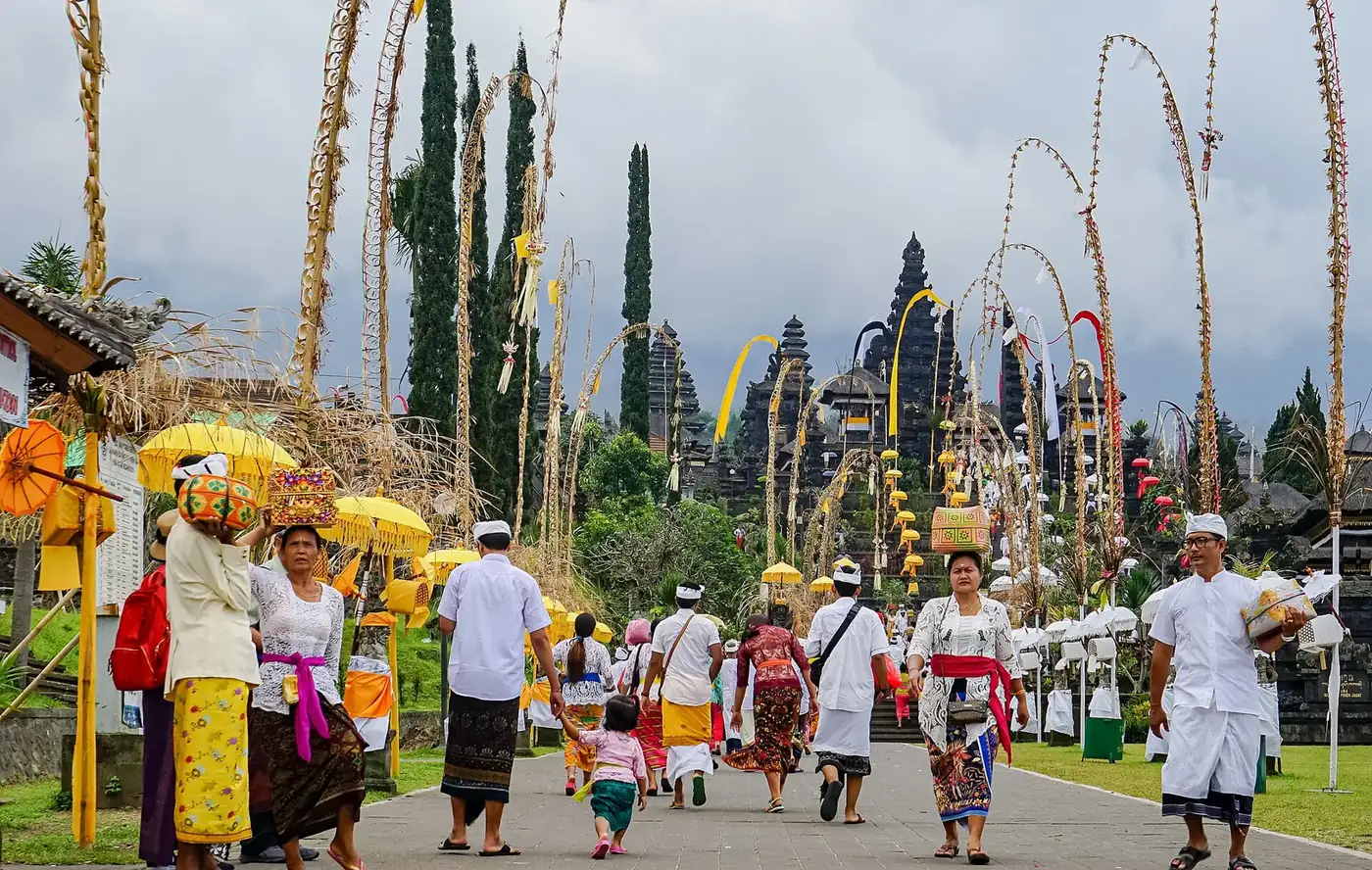 Balinese worshippers in ceremonial dress carrying offerings along the penjor-lined approach to Besakih on a festival day