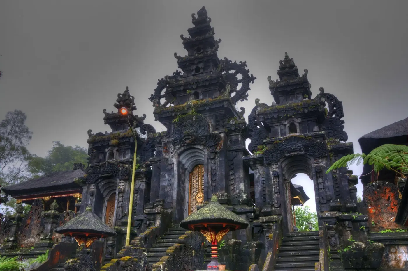Carved black volcanic stone gateways and steps at the Besakih temple complex under a grey sky