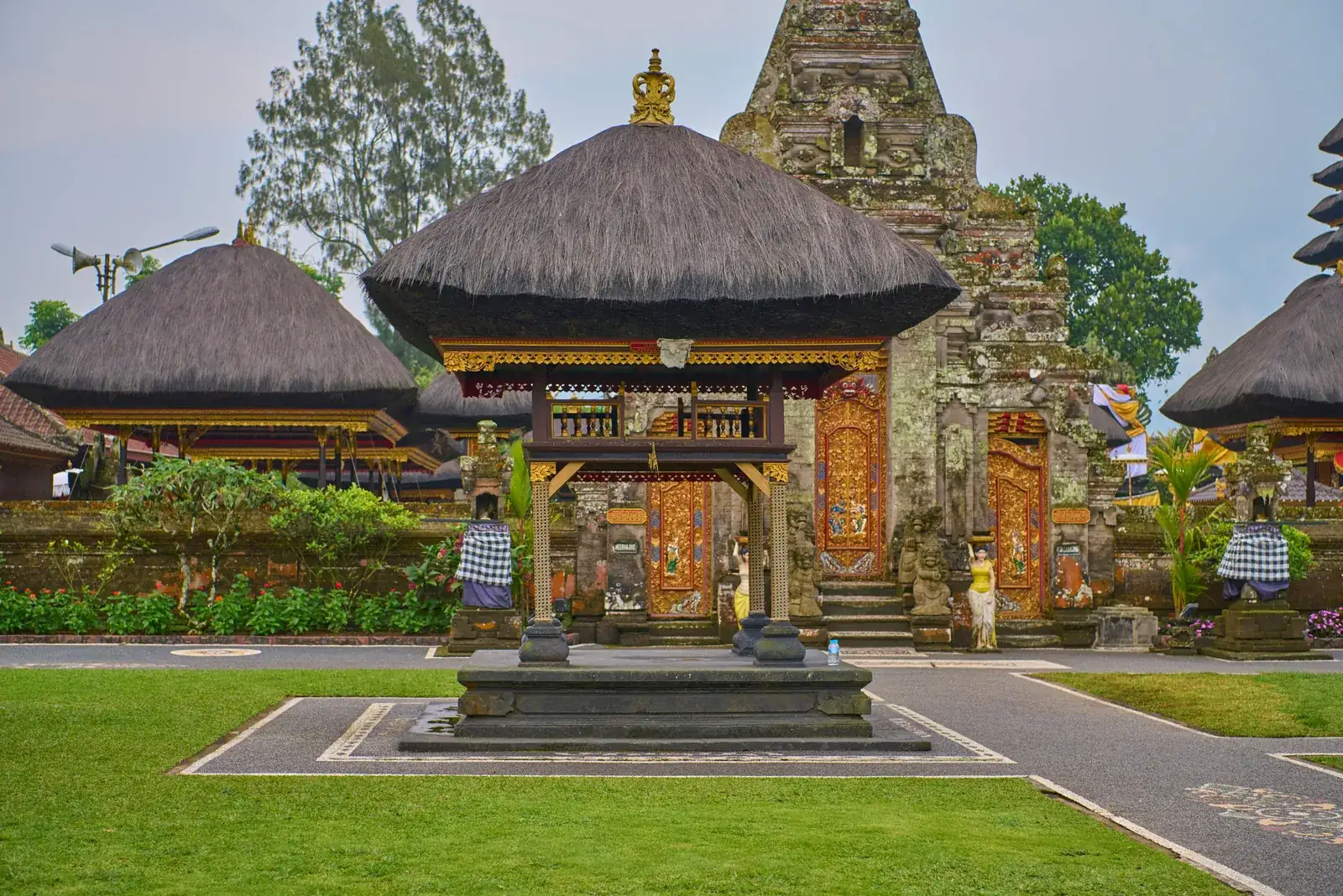 Gilded kori agung gate and thatched bale in the courtyard of a working Balinese temple