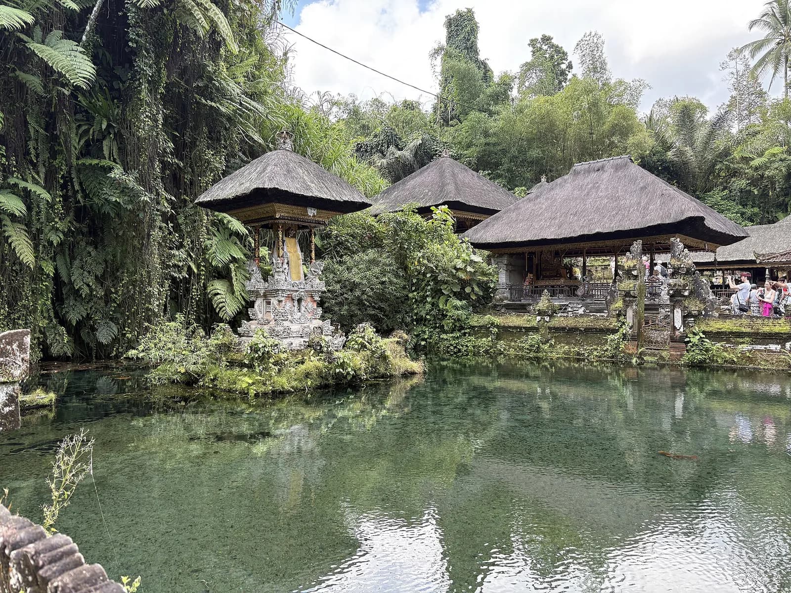 Clear water pool with island shrine and thatched pavilions at Pura Gunung Kawi Sebatu, Bali