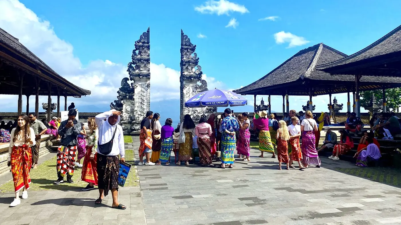 Visitors in rented sarongs queueing in front of the split gate at Lempuyang, on dry paving stones
