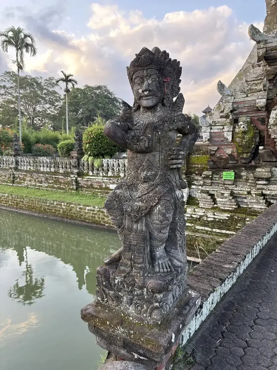 Carved stone guardian figure on the causeway parapet at Taman Ayun, with the moat behind it