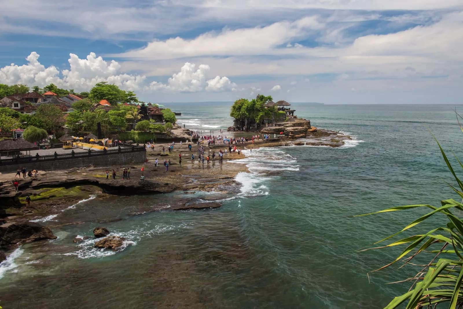 Visitors walking across the exposed rock shelf towards Tanah Lot temple at low tide, Beraban, Bali