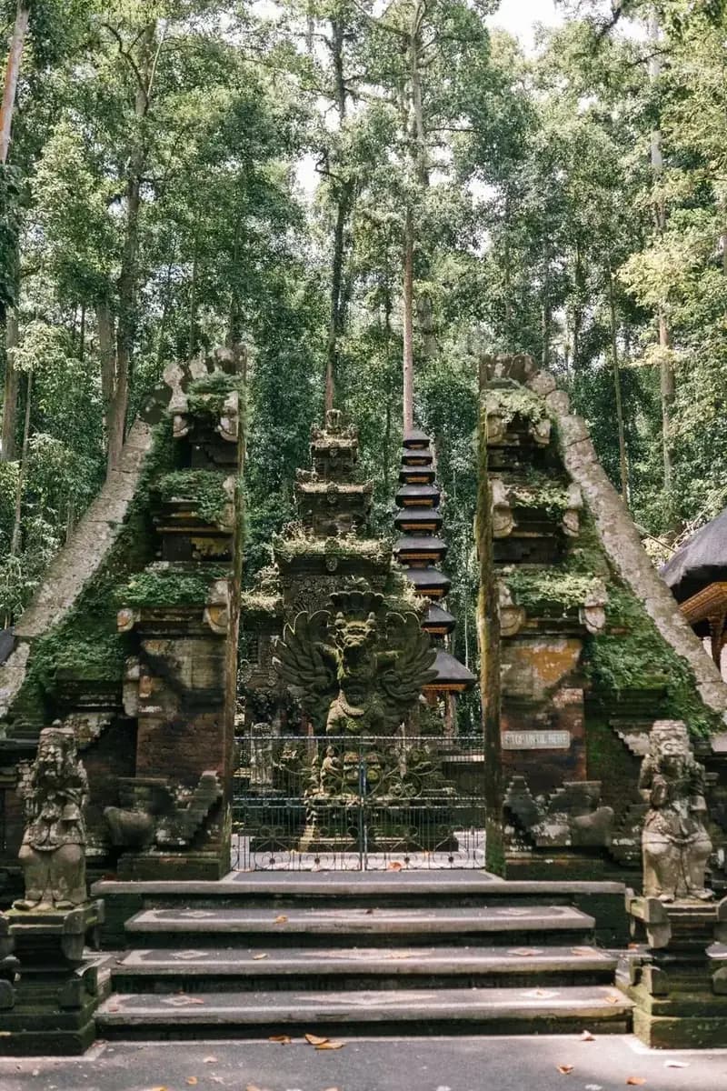 Mossy split gate and guardian statues at a forest temple in Bali