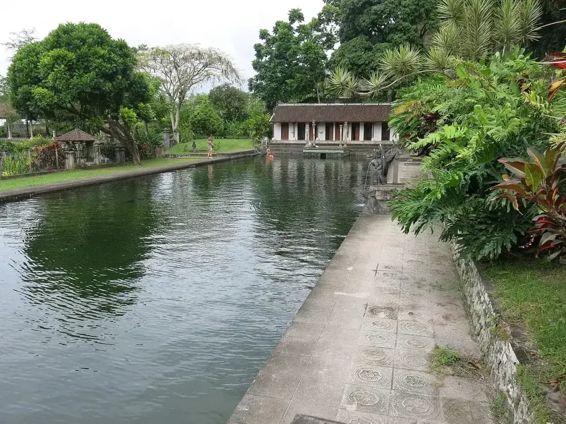 The long spring-fed bathing pool at the upper level of Tirta Gangga with swimmers and a pavilion behind