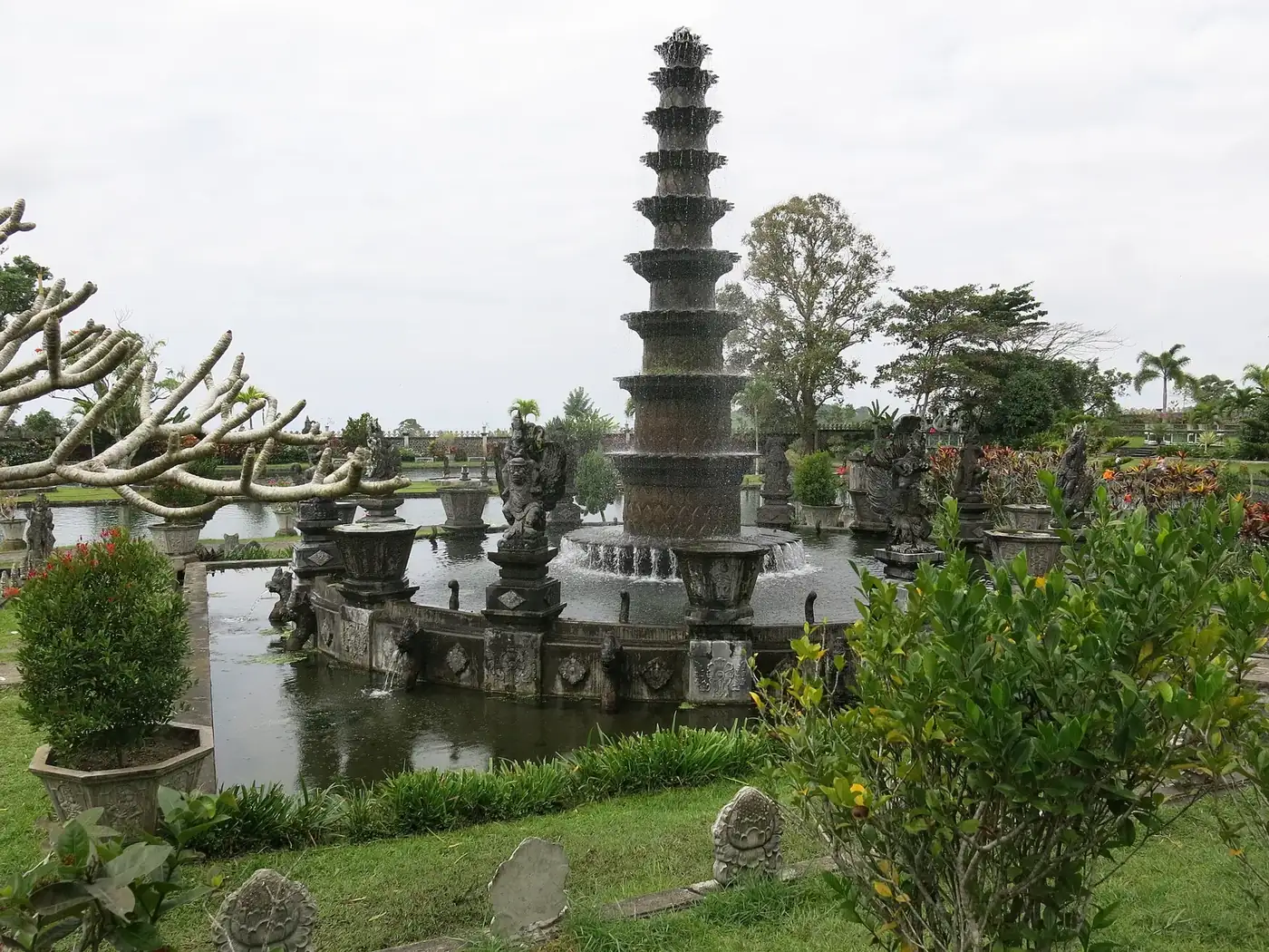 The eleven-tier stone fountain rising from its pond at Tirta Gangga, with statues and clipped garden beds around it