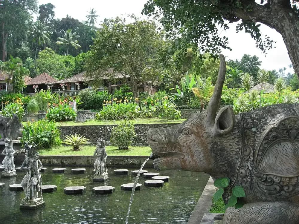 A carved bull spouting water into the stepping stone pond at Tirta Gangga, with the garden and pavilions behind