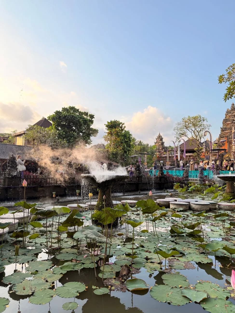 A fountain in the lotus pond at the Ubud Water Palace in the late afternoon, with the temple gates behind
