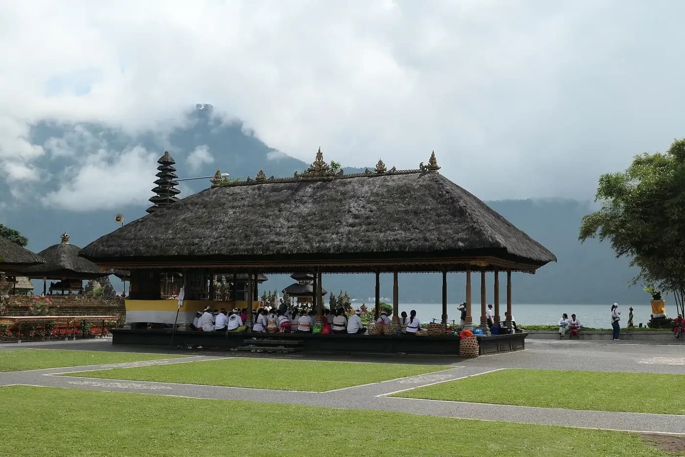 Worshippers in white seated in the open bale pavilion at Ulun Danu Beratan with cloud on the crater rim