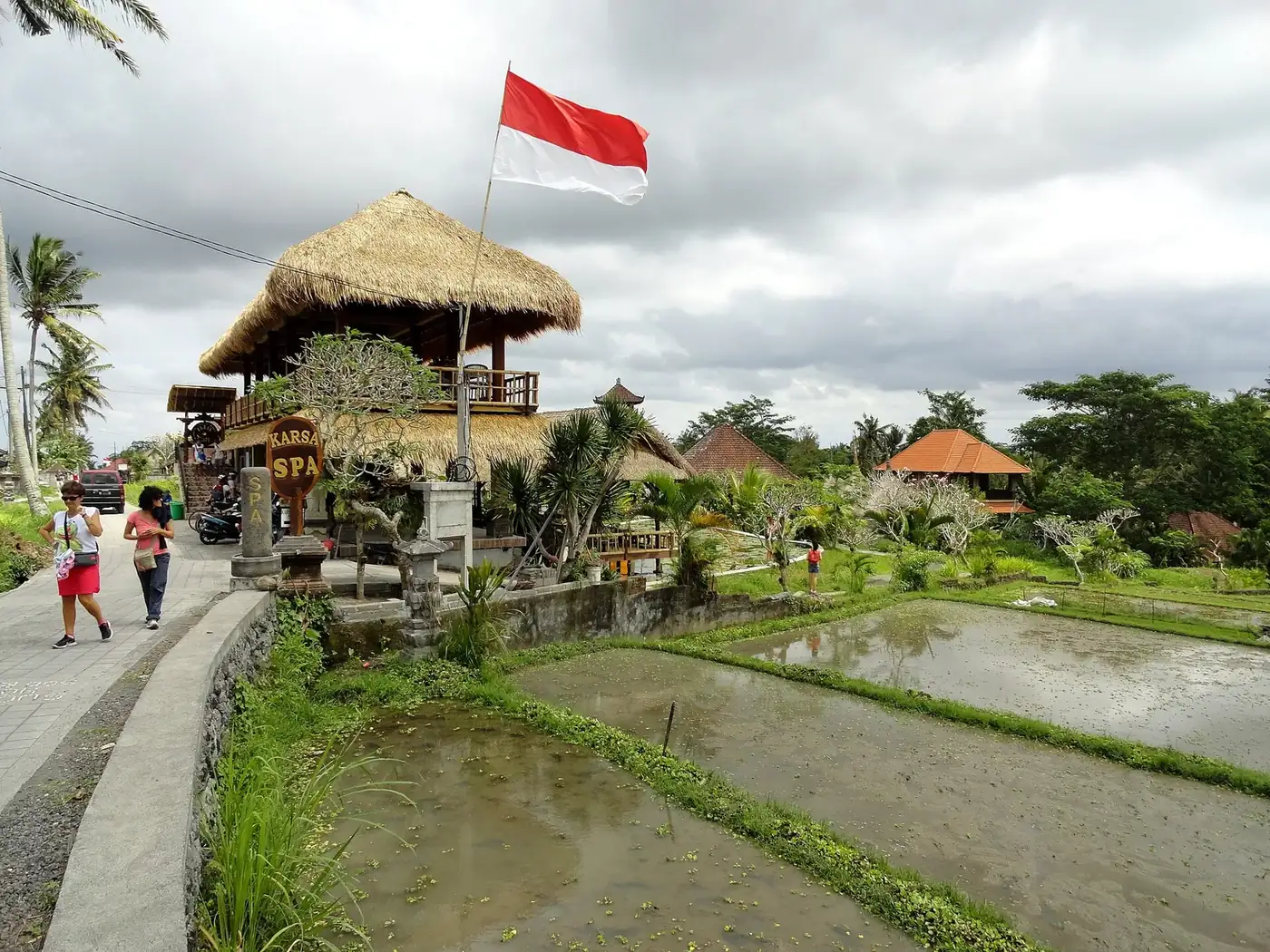 Walkers passing a thatched cafe and spa beside flooded rice paddies at Bangkiang Sidem, at the end of the Campuhan ridge