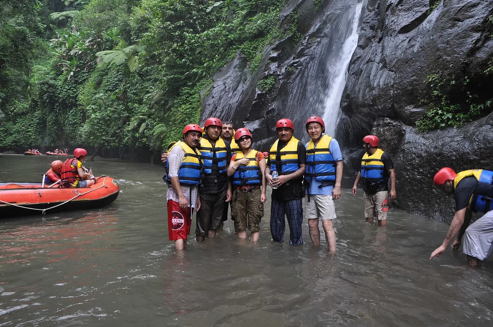 Rafters in helmets and life jackets standing in the Ayung River below a waterfall, Ubud, Bali