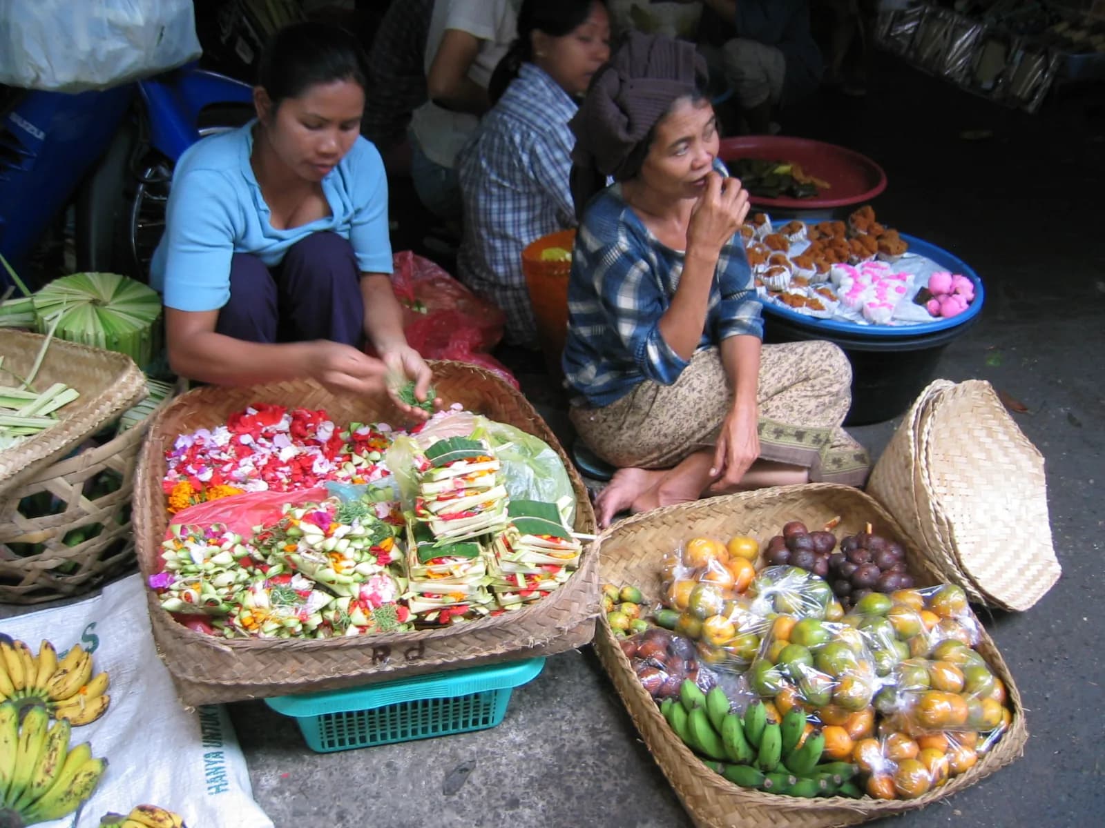 Women selling canang offerings, flower petals and fruit from woven baskets at the morning market in Ubud, Bali