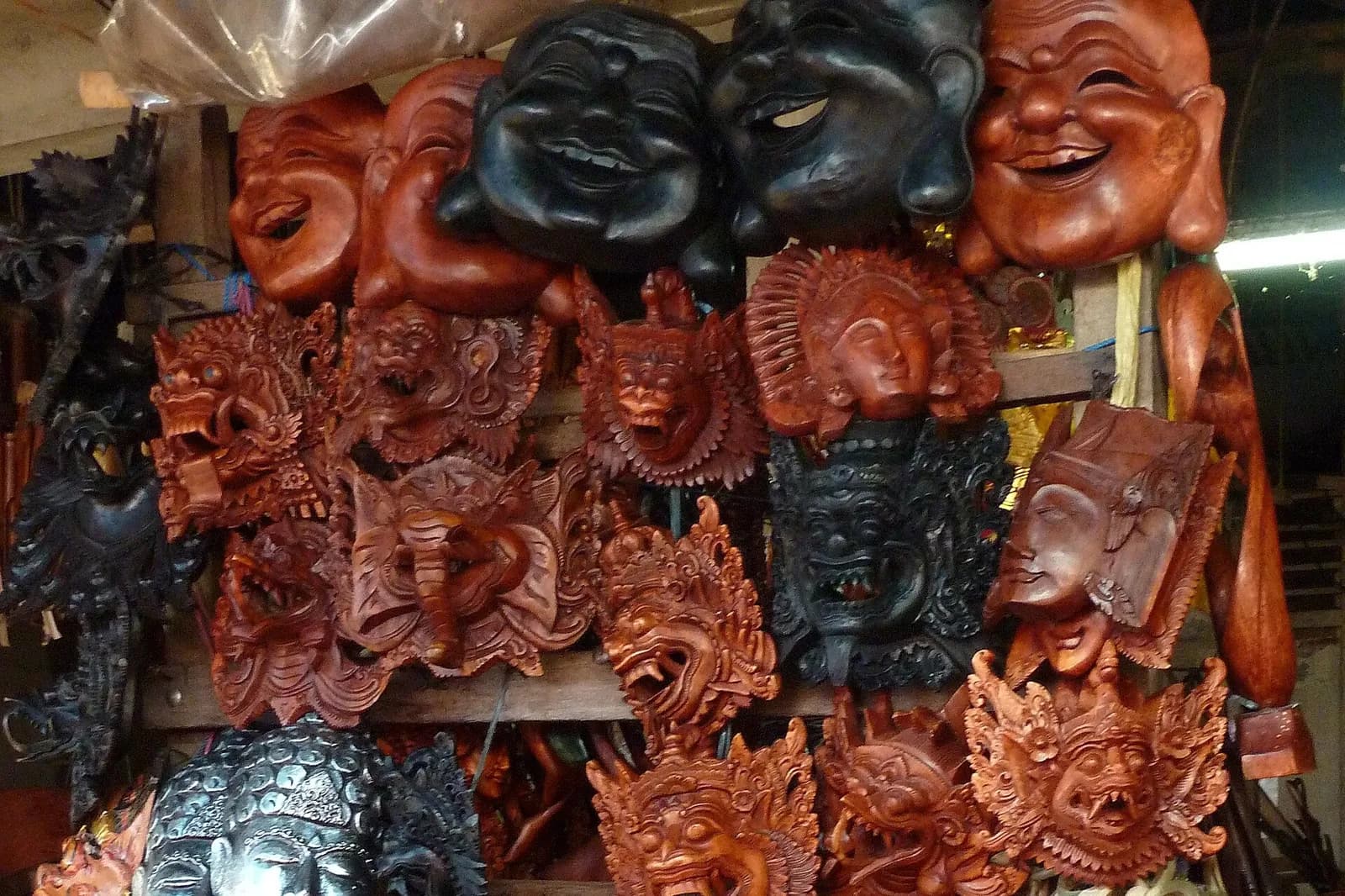Carved and painted wooden masks, including Barong-style faces, hung on a souvenir stall at Ubud Market