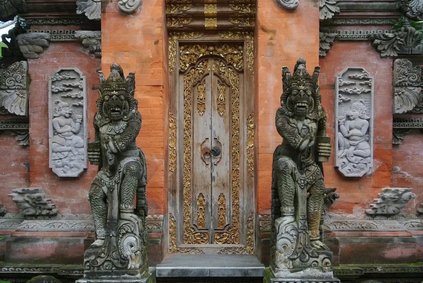 Carved and gilded doorway flanked by guardian statues at a Balinese palace gateway in Ubud