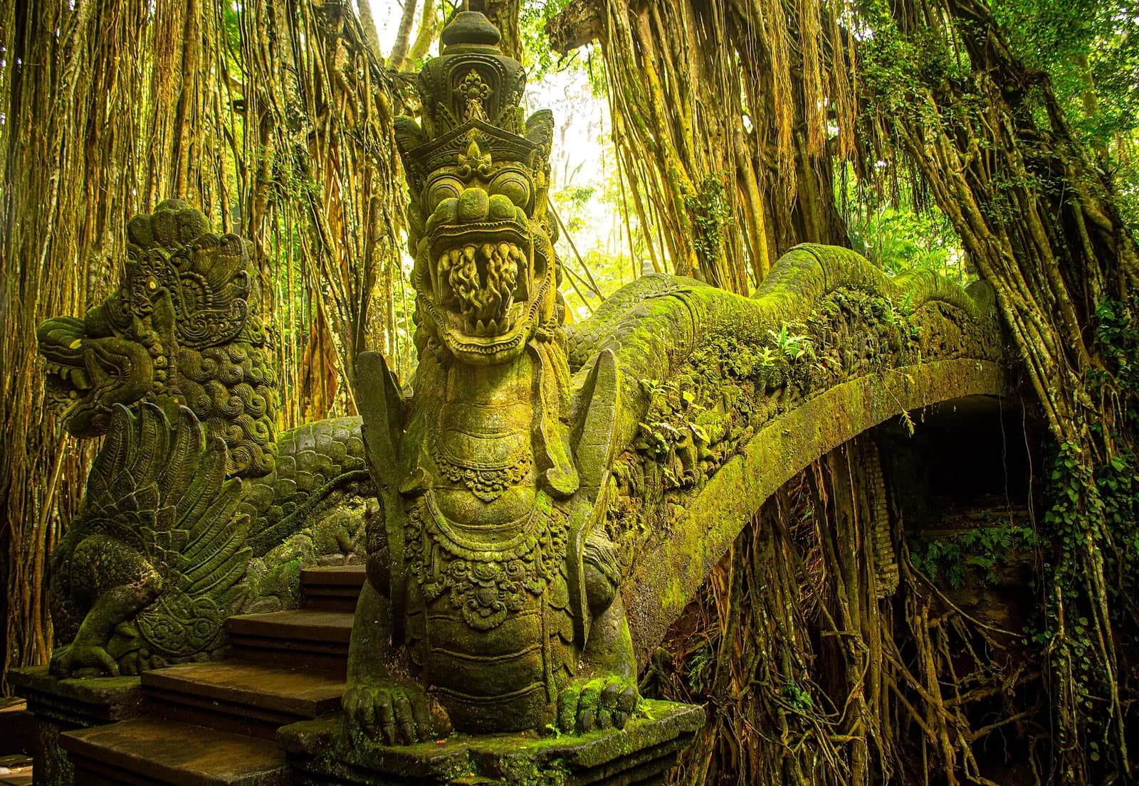 The moss-covered dragon bridge beneath hanging banyan roots in the ravine of the Sacred Monkey Forest, Ubud