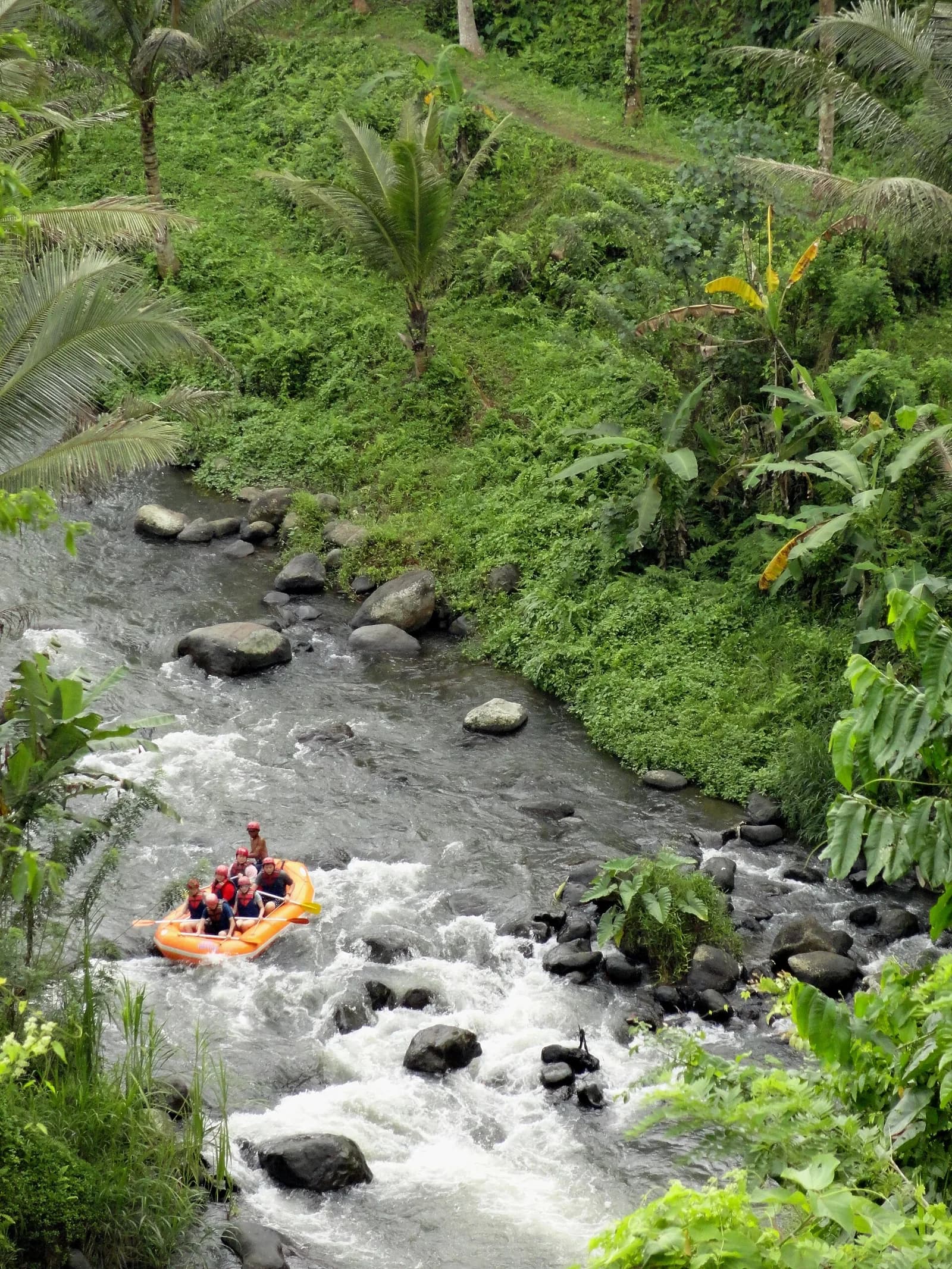 An orange raft running a rocky rapid on the Ayung River in the jungle below the Sayan ridge, Ubud, Bali