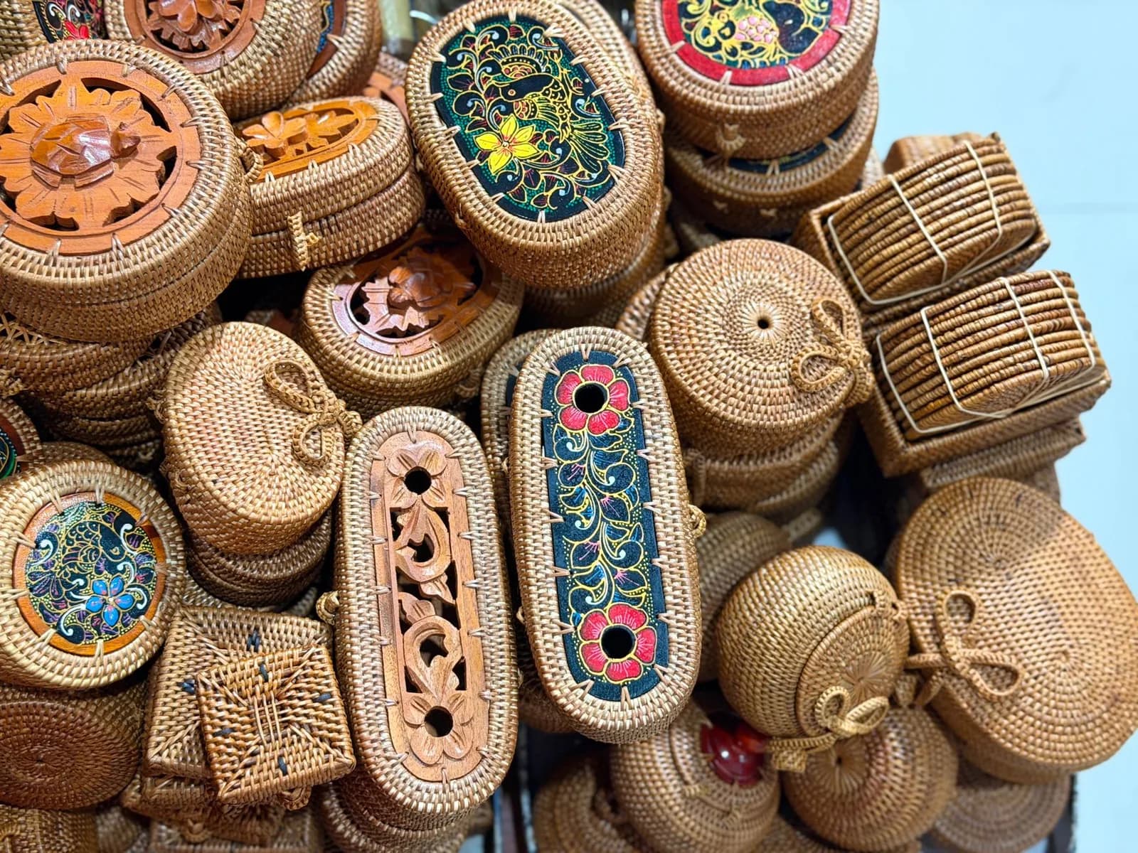 Pile of handwoven rattan bags with carved wood and hand-painted lids at a Bali handicraft stall