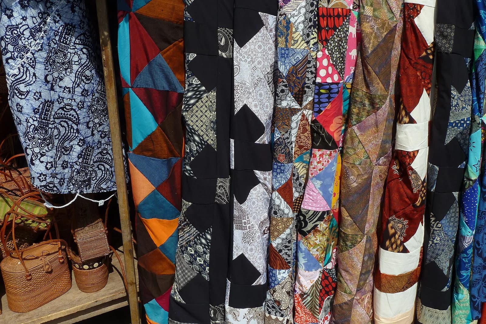 Batik and patchwork fabrics hanging beside woven rattan bags at a market stall in Ubud, Bali