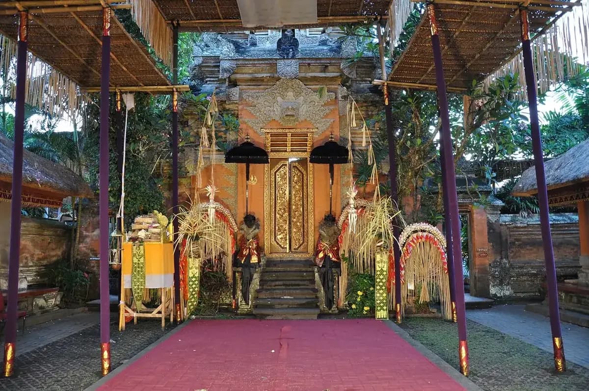 The Ubud Palace gateway dressed for a ceremony with penjor, offerings and a red carpet leading to the gold doors