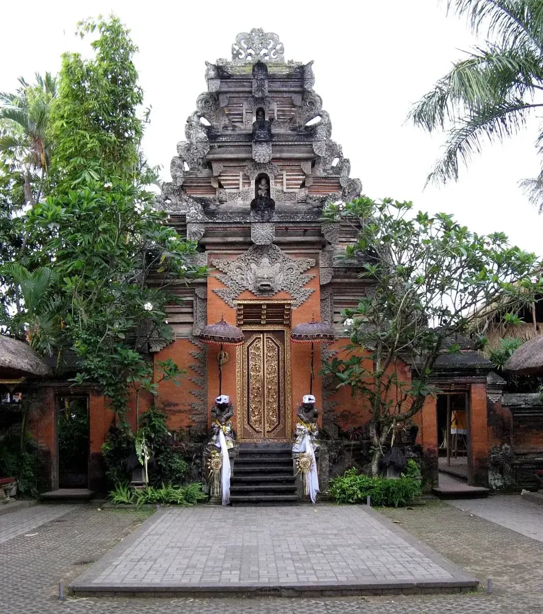 The carved brick and stone gateway of Ubud Palace with gilded doors and two guardian statues in ceremonial cloth
