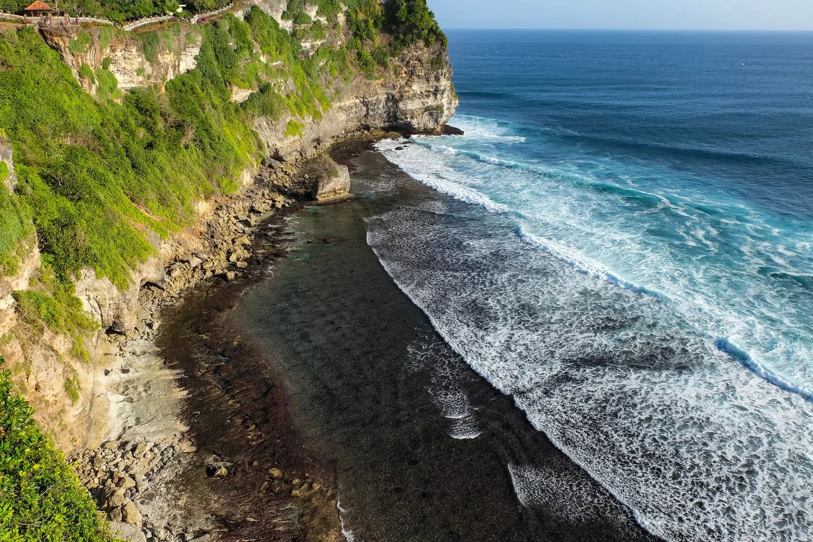 Looking down the cliff face at Uluwatu, Bali, to the rocky shore and surf line at the base