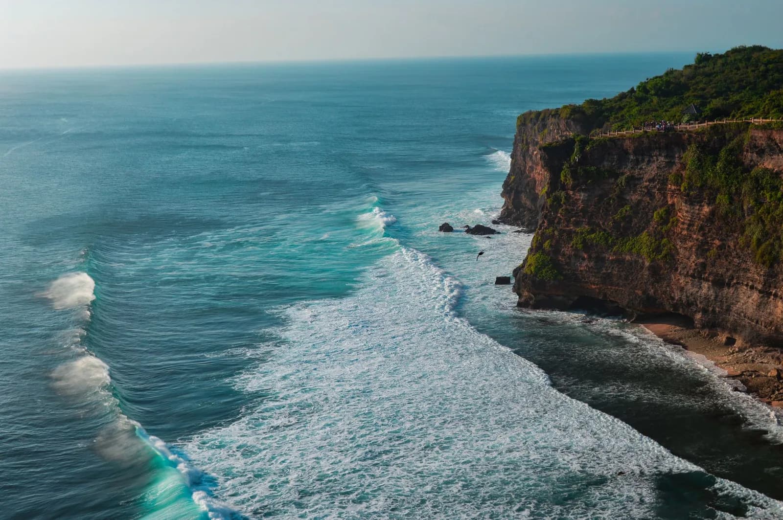 The cliff wall at Uluwatu, Bali, with a clifftop path along the rim and the reef break running below
