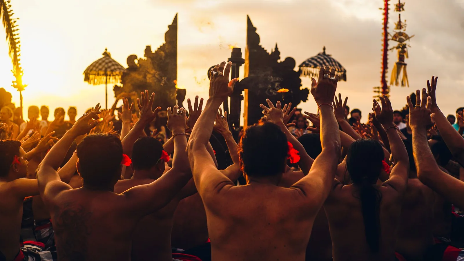 The kecak chorus with arms raised at sunset in front of the temple gate at Uluwatu, Bali