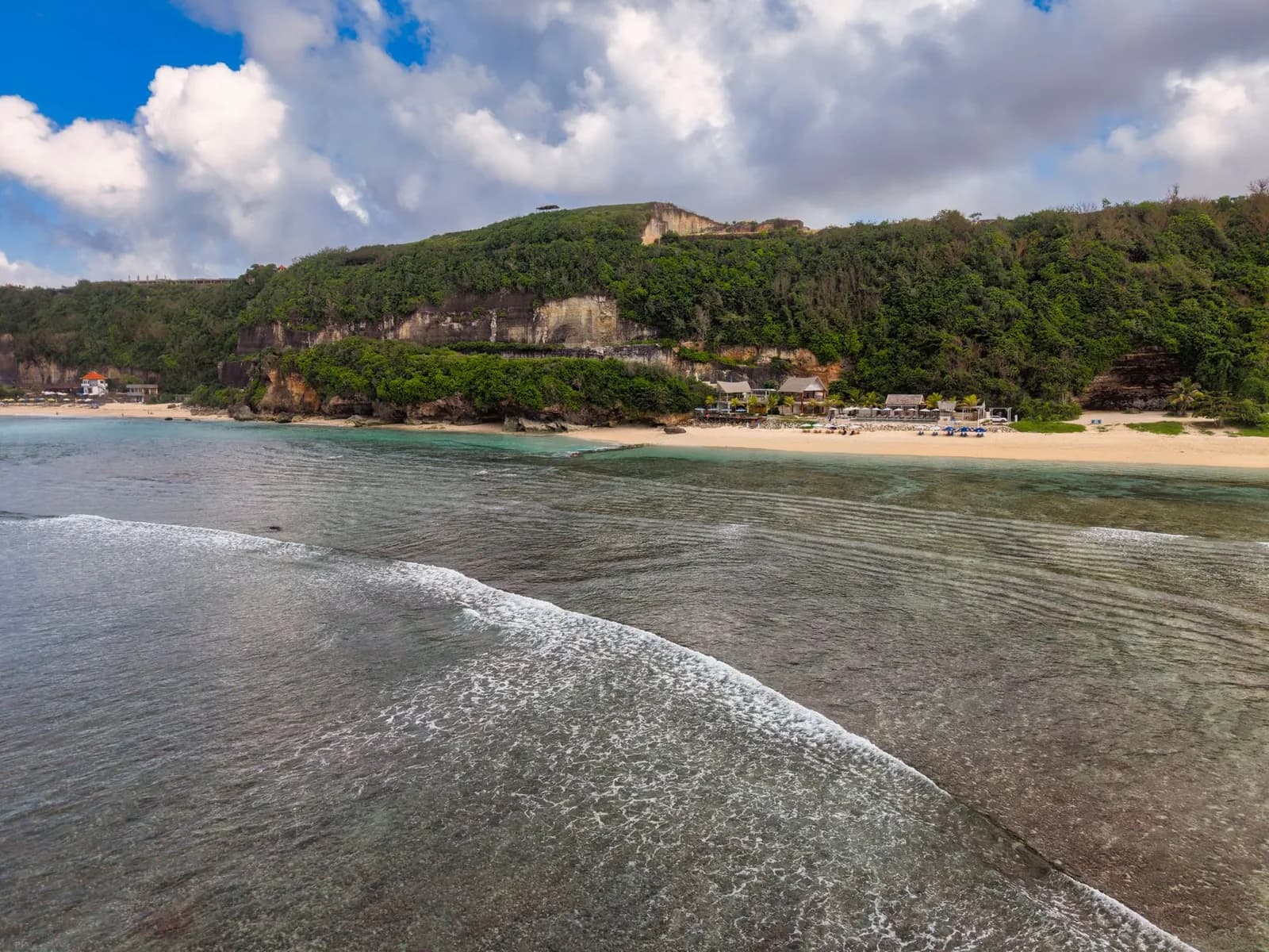 A wide beach below a white limestone cliff on the Bukit peninsula, Bali, with day beds along the sand