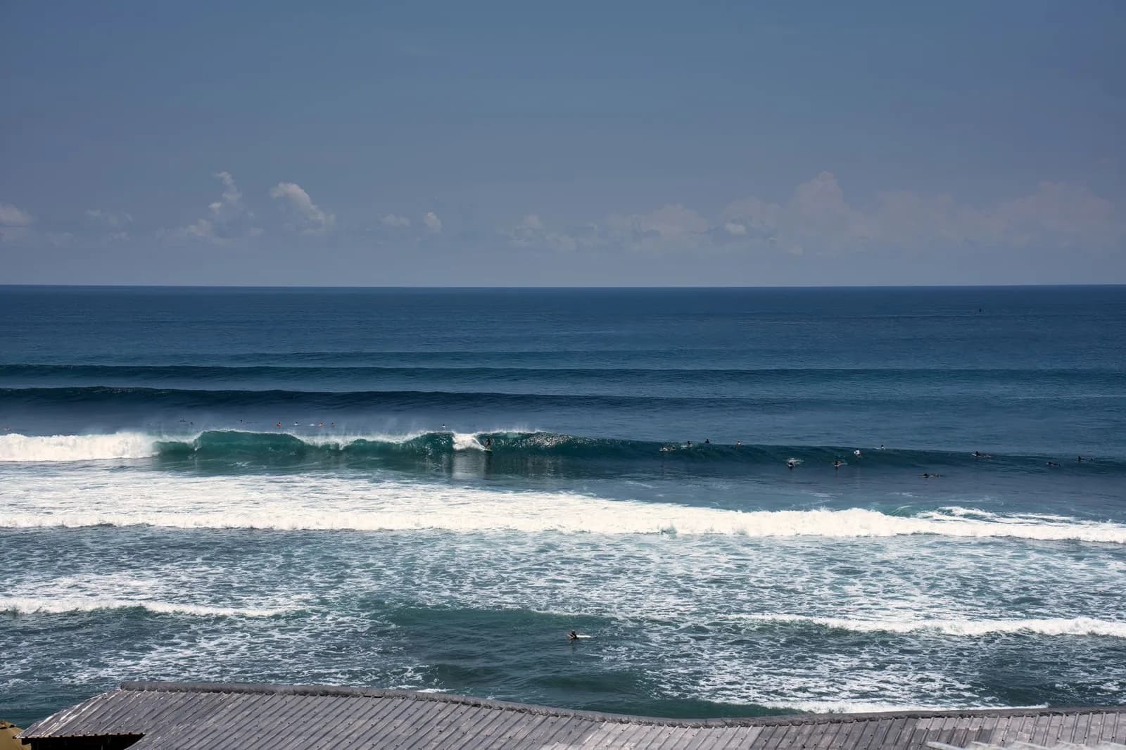 Surfers lined up along the reef break below the clifftop warungs at Uluwatu, Bali